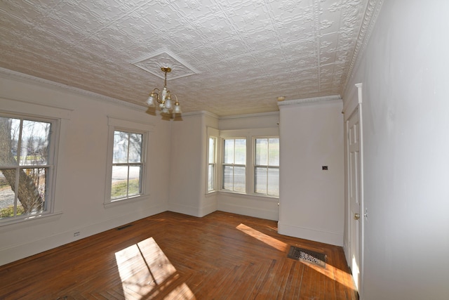 spare room with dark parquet flooring, a chandelier, a textured ceiling, and ornamental molding