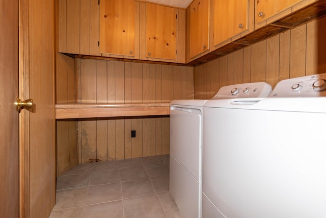 laundry room featuring washing machine and clothes dryer, wood walls, light tile patterned flooring, and cabinets