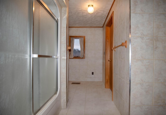 bathroom featuring tile patterned flooring, bath / shower combo with glass door, and tile walls