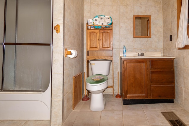 full bathroom with vanity, tile patterned floors, bath / shower combo with glass door, toilet, and tile walls