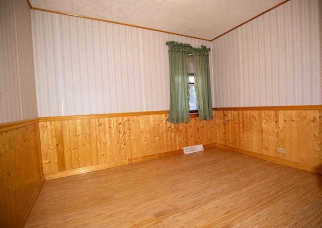 empty room featuring wood walls, wood-type flooring, and ornamental molding