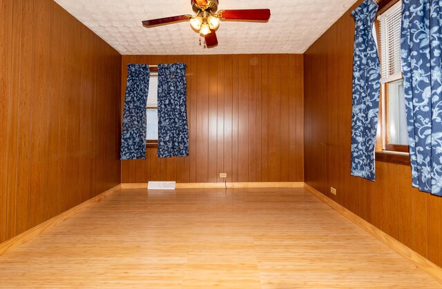 unfurnished room with light wood-type flooring, ceiling fan, and wood walls