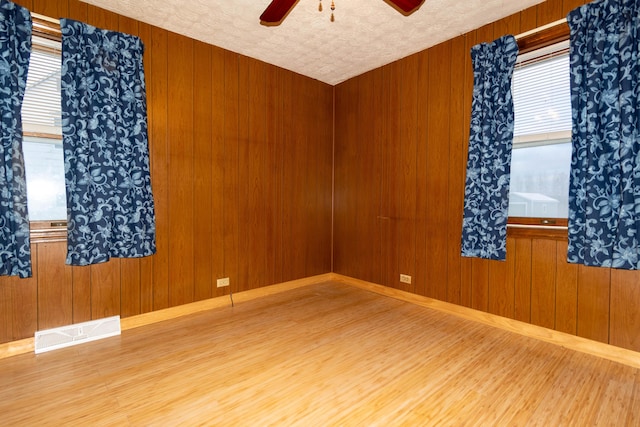 empty room with wood-type flooring, a textured ceiling, ceiling fan, and wooden walls