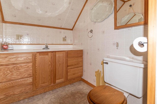 bathroom with tile patterned floors, lofted ceiling, toilet, vanity, and tile walls