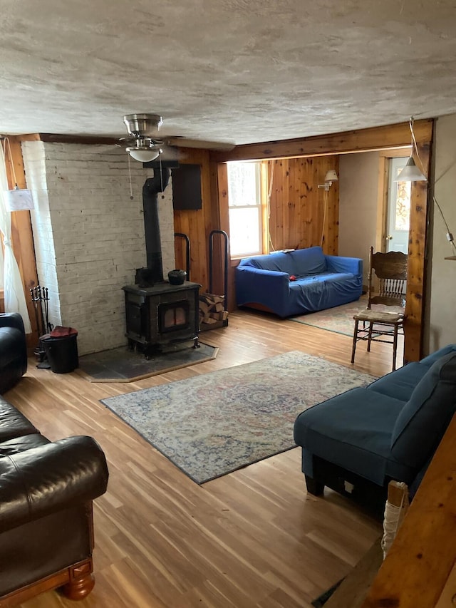 living room with a wood stove, ceiling fan, hardwood / wood-style floors, and wood walls