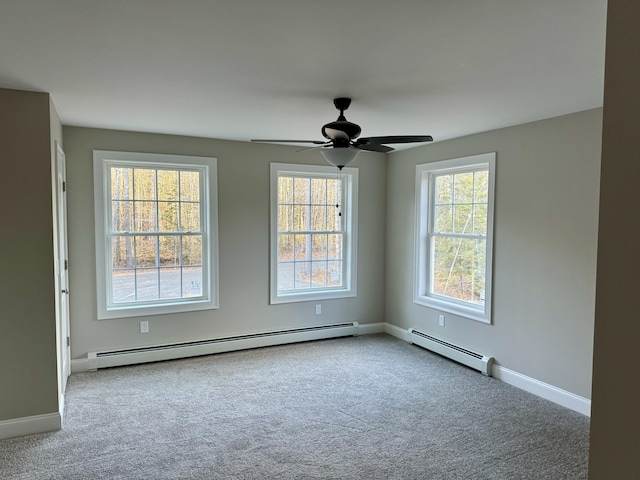 carpeted spare room featuring baseboard heating, ceiling fan, and plenty of natural light