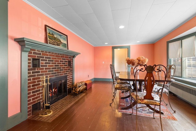 dining room featuring hardwood / wood-style floors, ornamental molding, radiator heating unit, and a brick fireplace