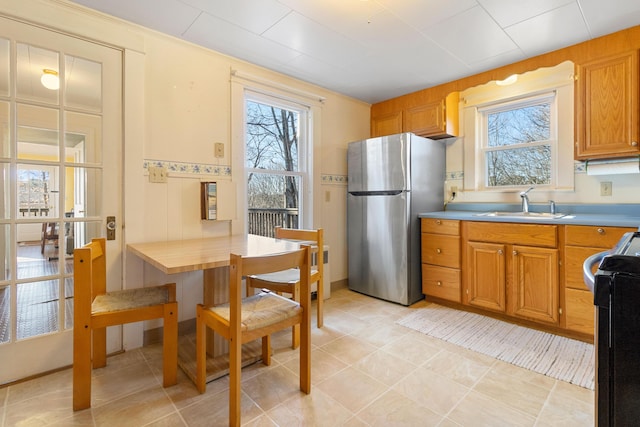 kitchen with a healthy amount of sunlight, stove, sink, and stainless steel refrigerator