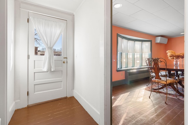 entryway with radiator heating unit, wood-type flooring, ornamental molding, and an AC wall unit