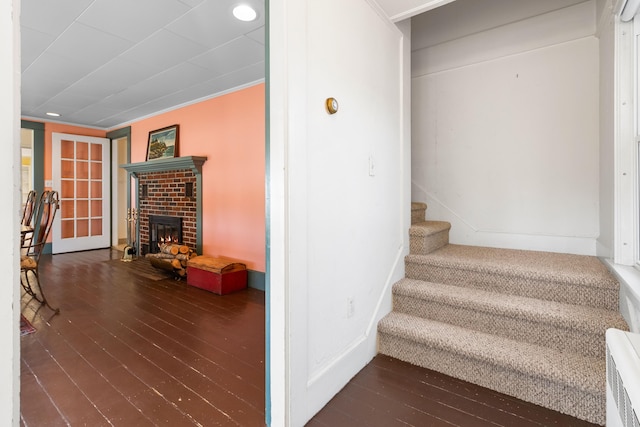 stairway with hardwood / wood-style flooring, radiator heating unit, ornamental molding, and a fireplace