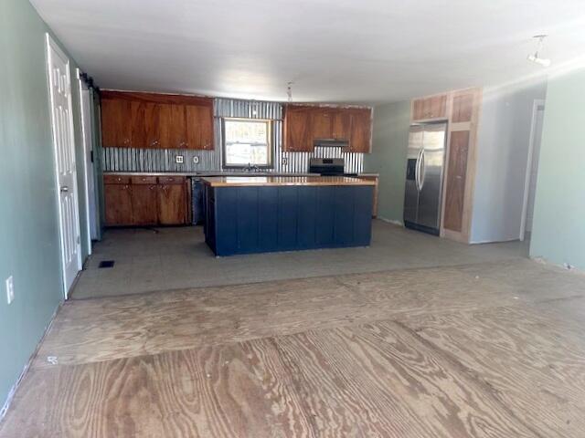 kitchen featuring stainless steel fridge, a kitchen island, stove, and range hood