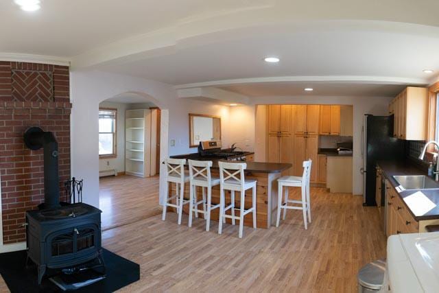 kitchen with a breakfast bar, light hardwood / wood-style floors, a wood stove, and sink