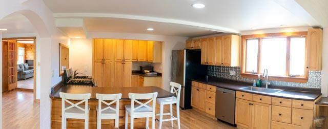 kitchen with decorative backsplash, appliances with stainless steel finishes, light wood-type flooring, a kitchen bar, and sink