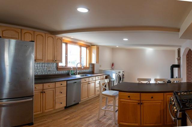 1 Branch St, Camden, ME 04843 - kitchen featuring stainless steel appliances, washing machine and clothes dryer, light wood finished floors, dark countertops, and decorative backsplash