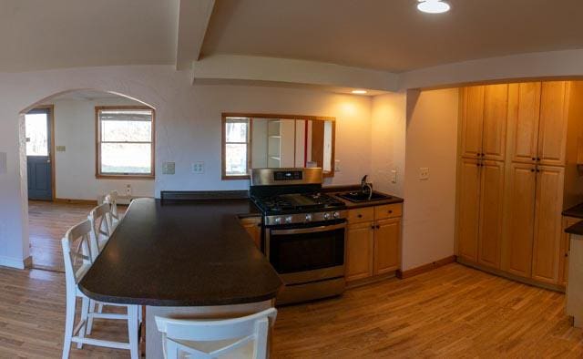 1 Branch St, Camden, ME 04843 - kitchen featuring stainless steel gas range oven, arched walkways, a peninsula, light wood-type flooring, and dark countertops