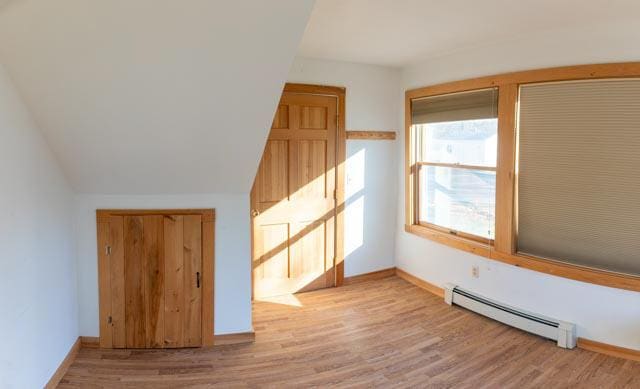 additional living space with baseboard heating, light hardwood / wood-style flooring, and lofted ceiling