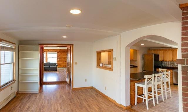 kitchen with appliances with stainless steel finishes, light wood-type flooring, a baseboard radiator, and tasteful backsplash