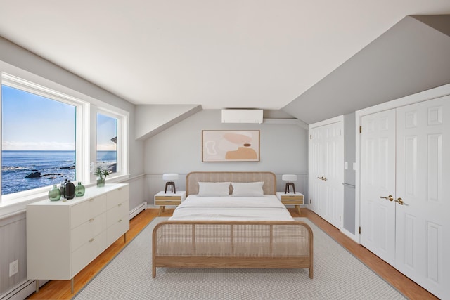 bedroom with a water view, multiple closets, baseboard heating, and light hardwood / wood-style flooring