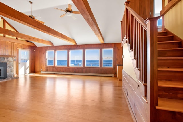 unfurnished living room with ceiling fan, light hardwood / wood-style flooring, beamed ceiling, a fireplace, and a water view