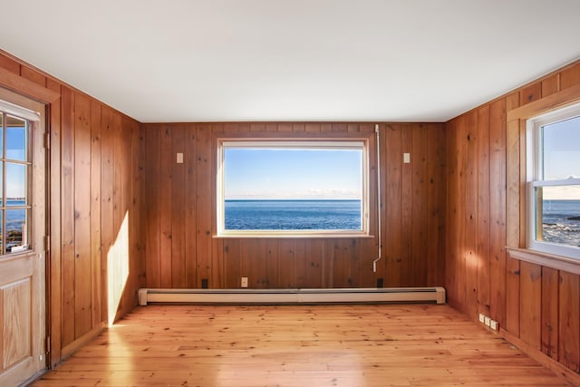 empty room with light wood-type flooring, a water view, baseboard heating, and wooden walls