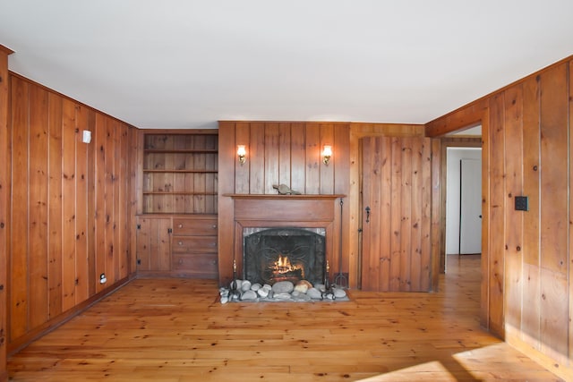 unfurnished living room with built in shelves, wooden walls, and light wood-type flooring