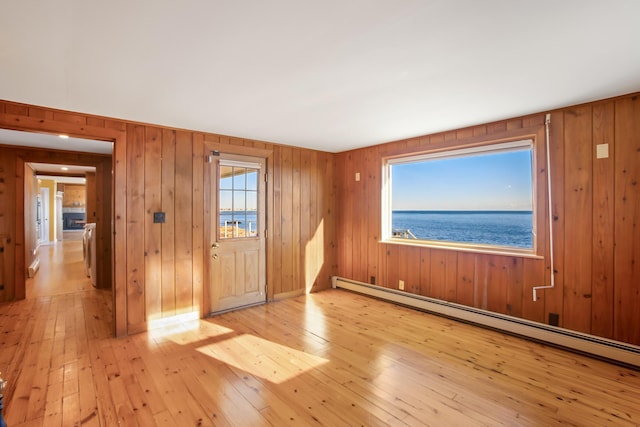 empty room featuring wood walls, a water view, a baseboard radiator, light hardwood / wood-style floors, and washer / dryer