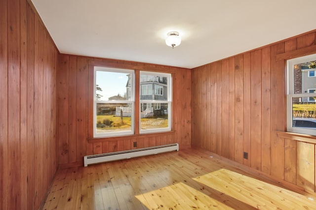 unfurnished room featuring wooden walls, light hardwood / wood-style floors, and a baseboard heating unit