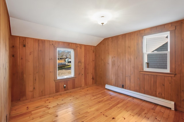 spare room featuring light wood-type flooring, a baseboard radiator, vaulted ceiling, and wooden walls