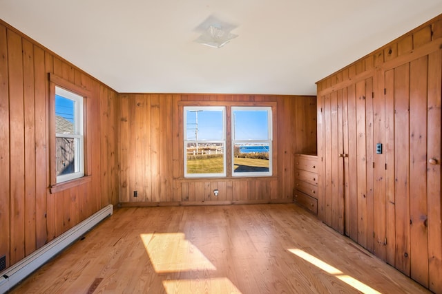 empty room featuring baseboard heating, wooden walls, and light hardwood / wood-style flooring