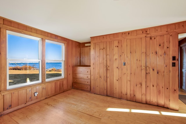 spare room with wood walls, light hardwood / wood-style flooring, and a water view