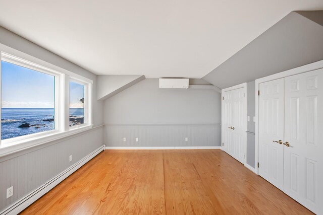 additional living space featuring hardwood / wood-style flooring, vaulted ceiling, a water view, and a baseboard heating unit