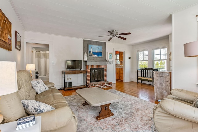 living room featuring wood-type flooring, a brick fireplace, and ceiling fan