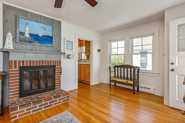 living area with wood-type flooring, a brick fireplace, baseboard heating, and crown molding