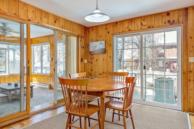 dining space featuring ceiling fan, light hardwood / wood-style flooring, wood walls, and a baseboard heating unit