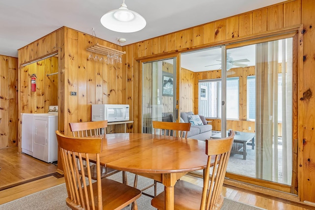 dining room featuring washer and clothes dryer, ceiling fan, light hardwood / wood-style floors, and wood walls