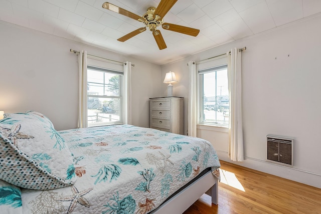 bedroom with multiple windows, ceiling fan, hardwood / wood-style floors, and heating unit