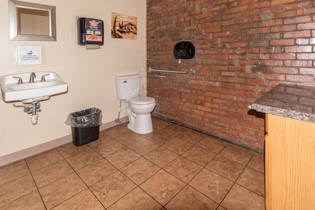 bathroom featuring toilet, sink, and brick wall