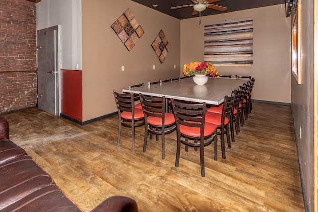 dining room with hardwood / wood-style floors, ceiling fan, and brick wall