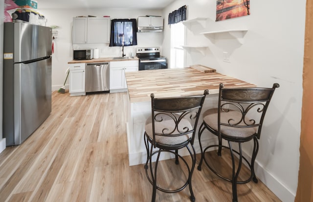 kitchen with butcher block countertops, white cabinetry, stainless steel appliances, and light hardwood / wood-style flooring