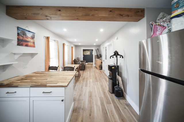 kitchen with wooden counters, light wood-type flooring, beamed ceiling, white cabinetry, and stainless steel refrigerator