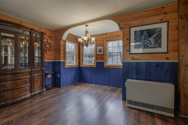 dining space featuring heating unit, wooden walls, dark wood-type flooring, and an inviting chandelier