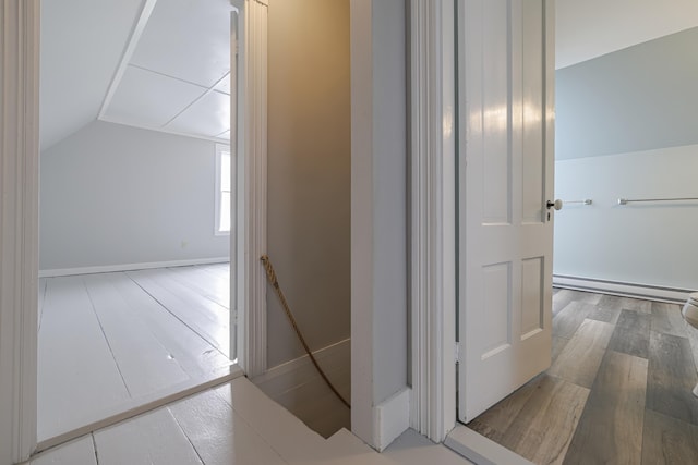 hallway featuring baseboard heating, wood-type flooring, and vaulted ceiling