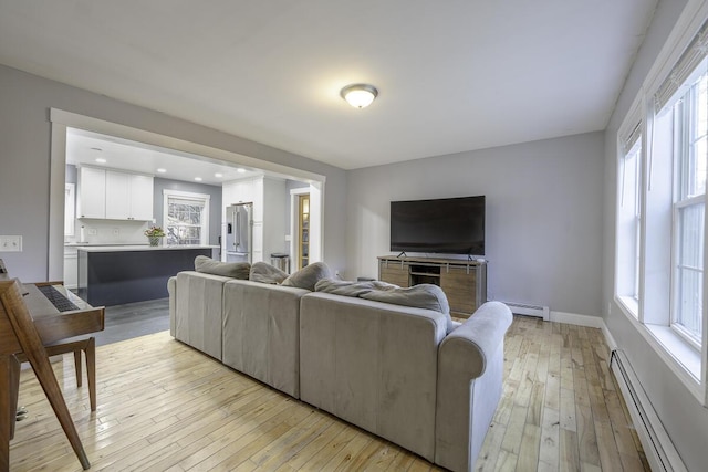 living room featuring baseboard heating, light hardwood / wood-style flooring, and a healthy amount of sunlight