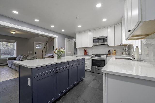 kitchen with sink, a kitchen island, light stone counters, white cabinetry, and stainless steel appliances