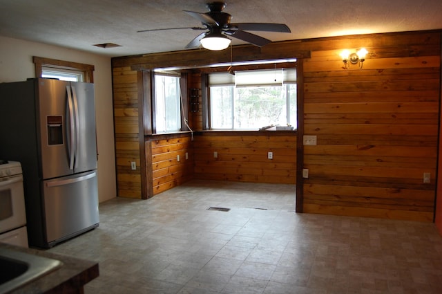 kitchen featuring ceiling fan, stainless steel refrigerator with ice dispenser, and wooden walls