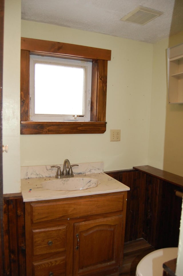 bathroom with a textured ceiling, vanity, and wooden walls