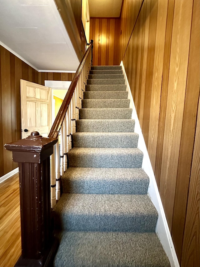 staircase featuring crown molding and wooden walls