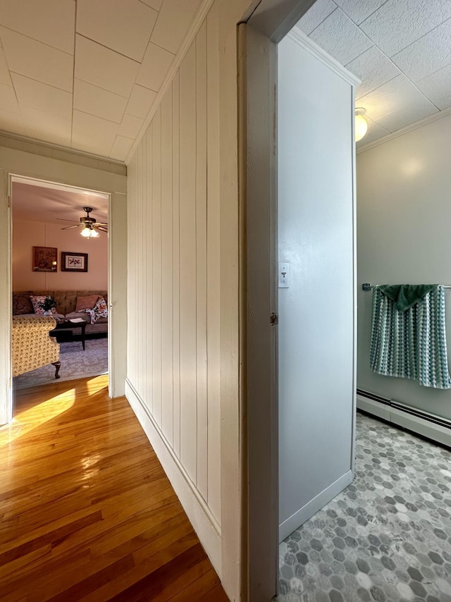 corridor with hardwood / wood-style flooring, crown molding, baseboard heating, and wood walls