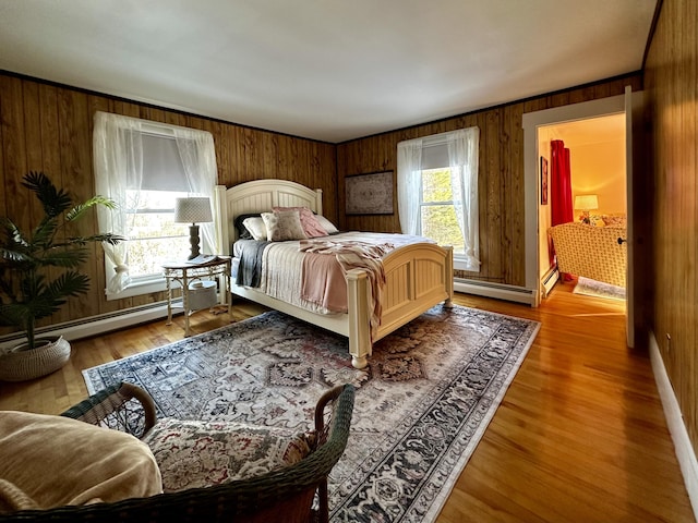 bedroom featuring hardwood / wood-style flooring, wooden walls, baseboard heating, and multiple windows