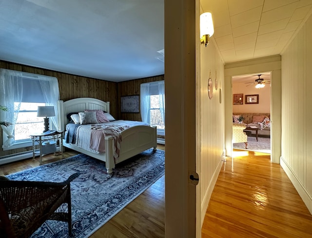 bedroom featuring a baseboard radiator, hardwood / wood-style floors, and wood walls